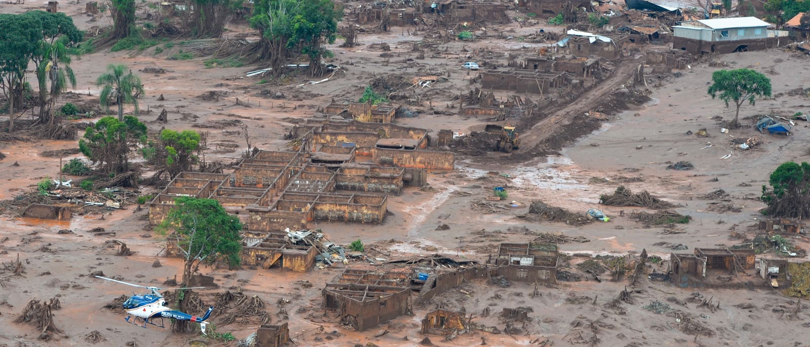 A wide aerial view of the destroyed village, with tailings covering the ground between the ruined buildings.